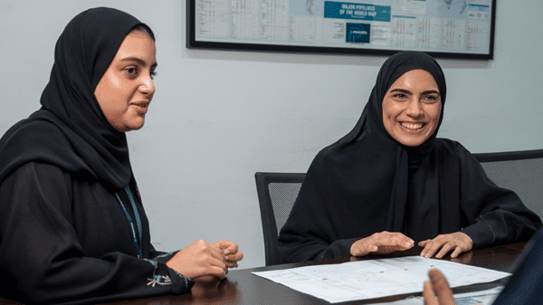 An image of two female Emirati graduates discussing a project over some engineering drawings